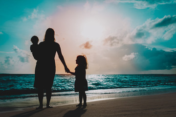 Wall Mural - mother with two kids walking on beach at sunset