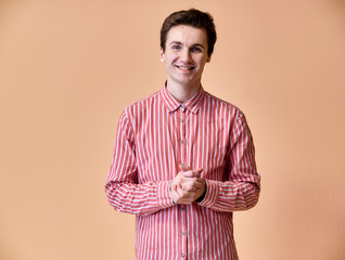 Portrait of a young Caucasian man with short hair and a white-toothed smile in a pink shirt on a pink background. Standing and talking right in front of the camera showing hands.