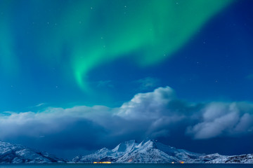 Aurora borealis, Tronso, Norway.  Green northern lights over Fjord And Mountains,  Night winter landscape with Starry sky and polar lights, aurora and snowy mountain in Background