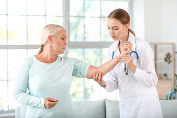 Doctor examining mature woman with joint pain at home