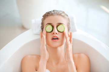 Beautiful young woman with cucumber slices lying in bathroom