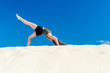 ein junges Mädchen macht im Sommer Yoga auf einer Düne im gelben Sand vor blauem Himmel 