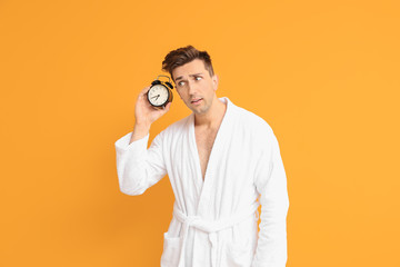 Poster - Emotional man in bathrobe and with alarm clock on color background