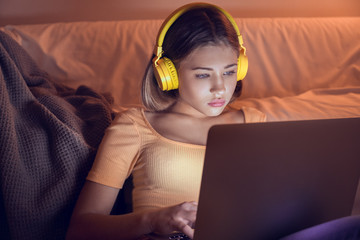 Teenage girl with laptop listening to music late in evening