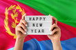 Eritrea New Year concept. Woman holding Happy New Year sign with hands on national flag background. Celebration theme.