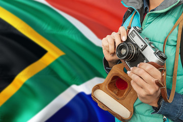 Wall Mural - South Africa photographer concept. Close-up adult woman holding retro camera on national flag background. Adventure and traveler theme.