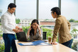 © kajonsakt - Young Asian businesswoman and businessman partners while working together discussing new project presentation before work business meeting withcomputer on wooden table background in office.