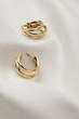 Subject shot of a pair of golden stud earrings isolated on the white textile surface. Each earring is made in the form of a triple unlocked hoop.
