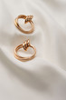 Subject shot of a pair of golden earrings isolated on the white textile surface. Each earring is made as a set of three glossy rings and a large double hoop