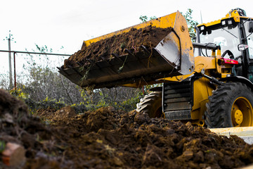 Excavation works at the construction site. Bulldozer or a backhoe loader dumping ground into the falsework. Low-rise construction. Foundation of  small cottage