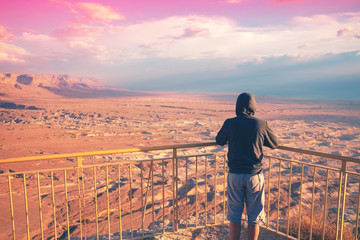 Wall Mural - Young man standing on a viewpoint on the mount (Masada) and gazing sunrise over the desert. The man looking at the valley. Israel