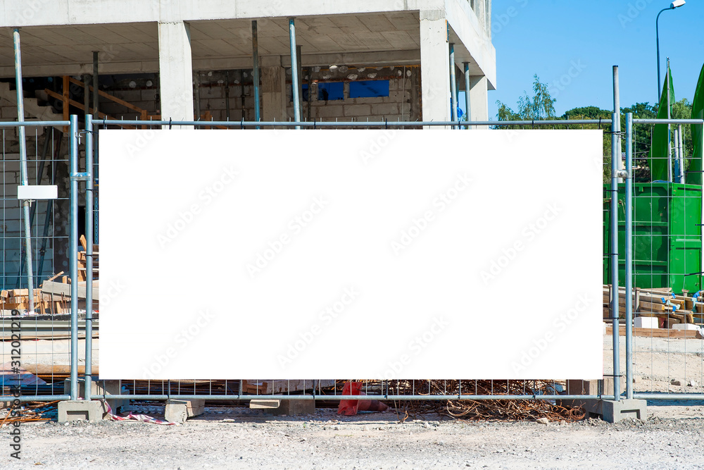 Blank white banner for advertisement mounted on the fence of construction site on a sunny day. - obrazy, fototapety, plakaty 