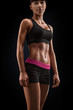 © USM Photography - Beautiful sexy female slim tanned body. Cheerful attractive young fitness woman in black top and black shorts isolated over black background