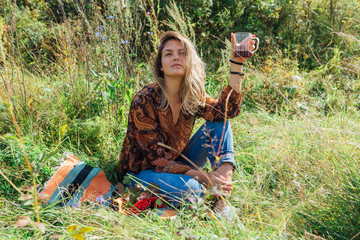 Beautiful woman sitting on the grass and drinking tea outdoors