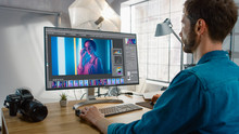 Professional Photographer Sitting At His Desk Uses Desktop Computer In A Photo Studio Retouches. After Photoshoot He Retouches Photographs Of Beautiful Female Model In An Image Editing Software