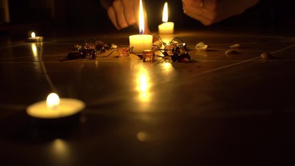 Wall Mural - A female hand collects shells and stones, white candles burn in a pentagram on a wooden floor. Magical ritual with occult, evil and esoteric symbols. Halloween Scary Rite