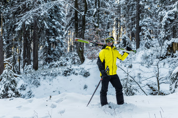 skier in goggles holding ski sticks and skis and standing near firs