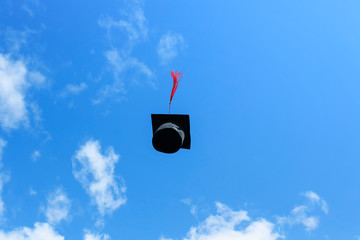 black student hat with red tassel tossed high in the blue sky on holiday graduation