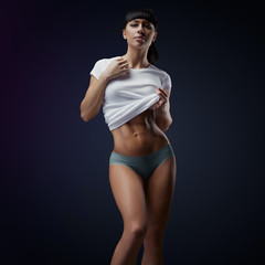 Wall Mural - Image of fitness woman in sports clothing, short sleeve tee, t-shirt, briefs. Fitness athletic young woman showing her well trained body, six pack, perfect abs, shoulders, biceps, triceps and chest.