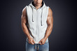 Close up photo of attractive fitness man wearing blank light gray sleeveless hoodie. Studio shot on dark background. Perfect fit, abdominal muscle, shoulders, deltoids, biceps.