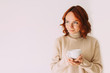 © Romanova - Lifestyle image of red haired beautiful girl sipping coffee from a white mug, wearing cozy sweater of a pastel color. Looking aside. Copy space.