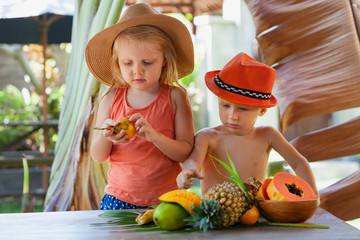 Photo of funny siblings. Couple of happy children with smiling face eating exotic tropical fruits. Healthful food, natural picnic on luxury resort. Healthy lifestyle on summer family holiday with kids