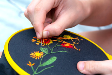 Wall Mural - Women's hand embroidery in a hoop, a woman embroider a pattern on dark material. Close-up. The concept of needlework, hobby, leisure.