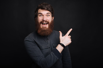 Wall Mural - Amazed young bearded man pointing away at copyspace