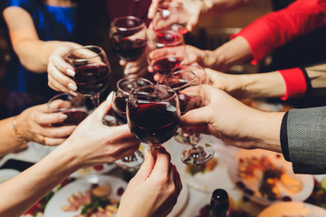 Close up shot of group of people clinking glasses with wine or champagne in front of bokeh background. older people hands.