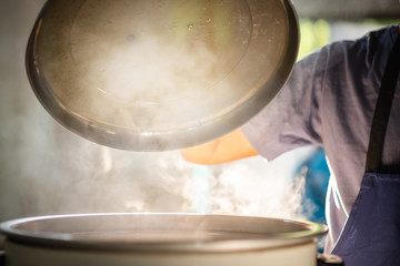 Wall Mural - The chef is opening the lid of the rice cooker, the mass of steam reflected in the morning light coming out of a large electric rice cooker heated in the cafeteria.