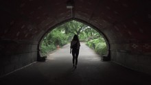 Lady Walking Under A Tunnel And Into Central Park In New York City. This Was Taken At A Regular Speed With Natural Motion Blur.