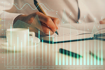 Double exposure of man's hands writing notes of stock market with forex chart.