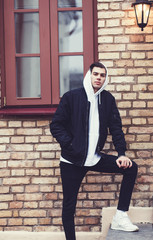 Wall Mural - cool men in jeans, jacket and white sneakers against a brick building