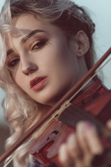 Wall Mural - face of a beautiful girl with a violin under her chin outdoors, young woman playing a musical instrument on nature in solitude, concept music and feelings