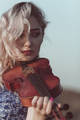 Wall Mural - face of a beautiful girl with a violin under her chin outdoors, young woman playing a musical instrument on nature in solitude, concept music and feelings