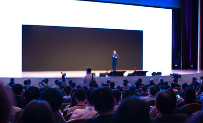 Fototapete - Speaker on the stage with rear view of audience in the conference hall or seminar meeting, business and education concept. Speaker giving a talk at business meeting. Seminar presentation photo.