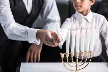 Wall Mural - Cropped view of Jewish father and son holding candle in apartment