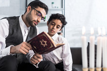Handsome Jewish Father And Son Reading Tanakh In Apartment