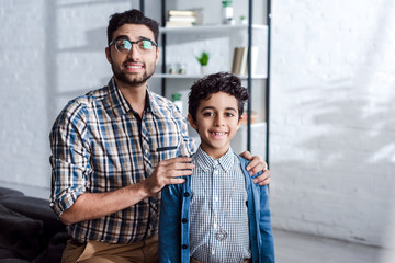 Wall Mural - smiling jewish father hugging son and looking at camera in apartment