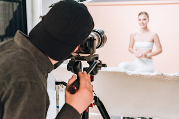 Wall Mural - Selective focus of cameraman shooting smiling model in photo studio