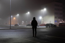 Woman Stands Alone At Parking Lot. City Landscape At Foggy Night. Long Exposure. Light Trails.