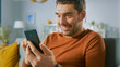 © Gorodenkoff - Portrait of Handsome Excited Man at Home Uses Smartphone. Man Relaxing with Mobile Phone in His Cozy Living Room.