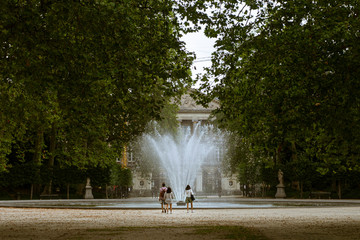 Royal Brussels Park in summer. Three people (one man, and two women) walking to a fountain.