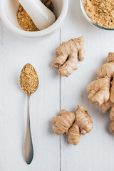 Natural ginger, ginger powder, mortar with chopped ginger and a spoon on the table