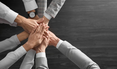 People holding hands together over grey wooden background, top view. Unity concept