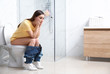 © New Africa - Upset woman sitting on toilet bowl in bathroom