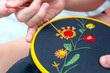 Women's hand embroidery in a hoop, a woman embroider a pattern on dark material. Close-up. The concept of needlework, hobby, leisure.