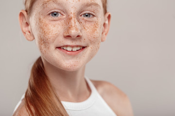 Wall Mural - Inclusive Beauty. Girl with freckles standing isolated on grey smiling playful close-up