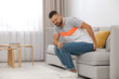 © New Africa - Man suffering from hemorrhoid on sofa at home