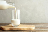Kefir, milk or Turkish Ayran drink are poured into a glass cup from a bottle. A glass stands on a wooden stand on a rustic wooden table. Place for text